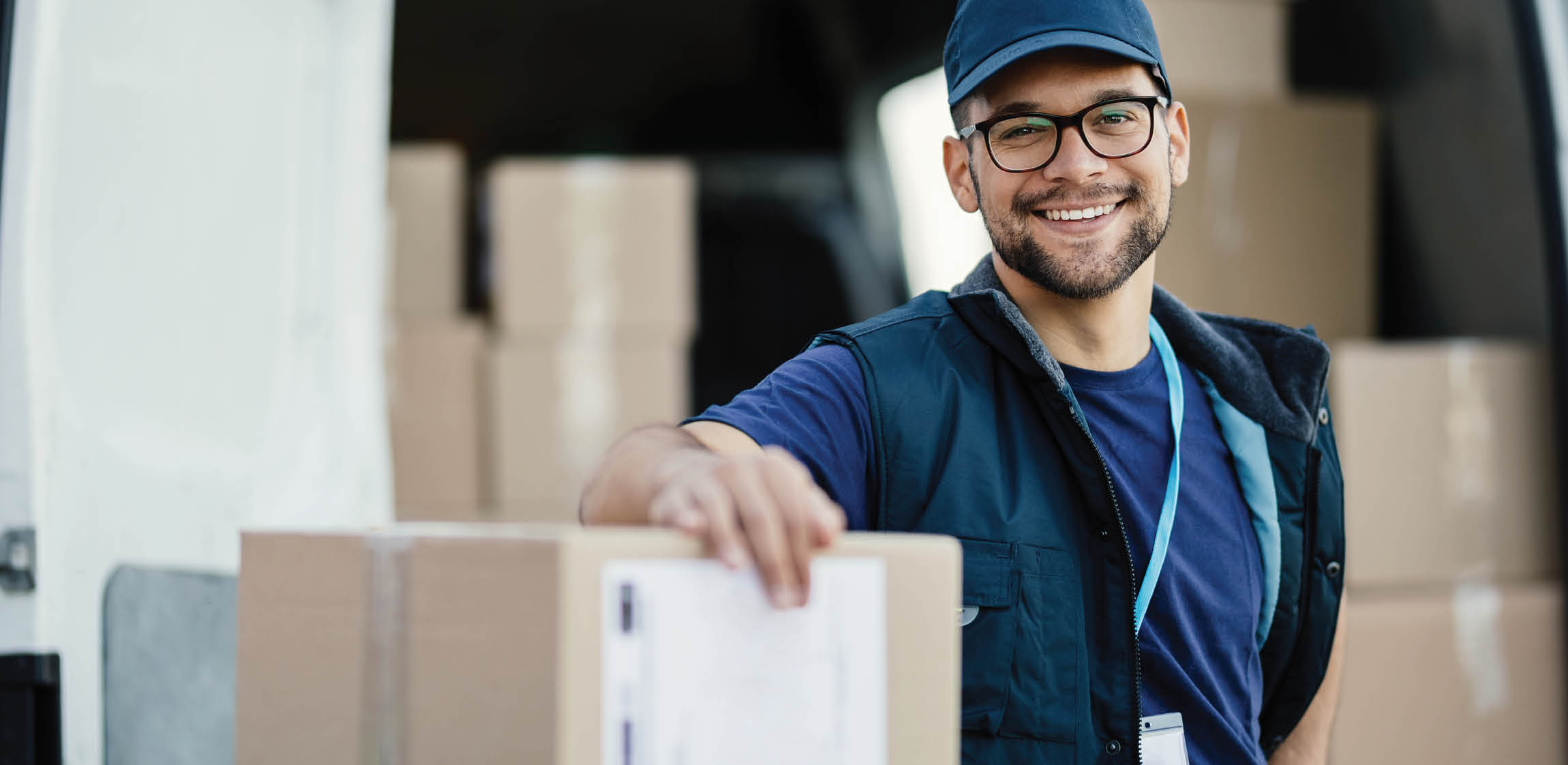 Portrait of happy worker unloading boxes from a delivery van and looking at camera 